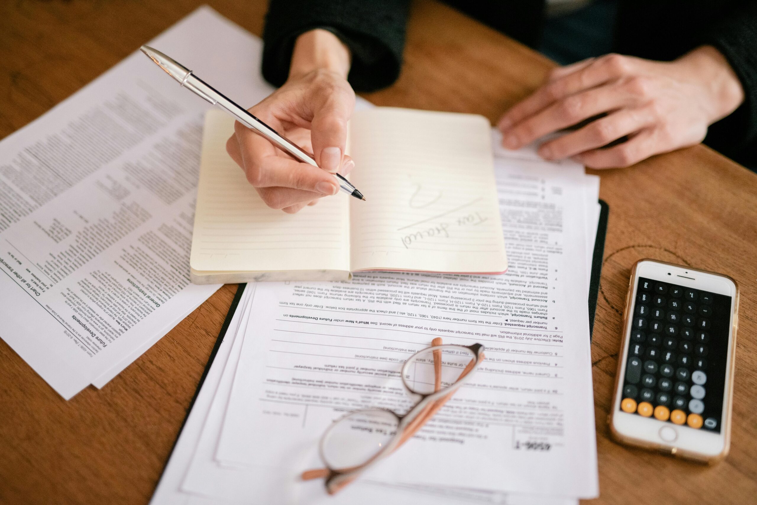 Person writing in a notebook with documents in front of them