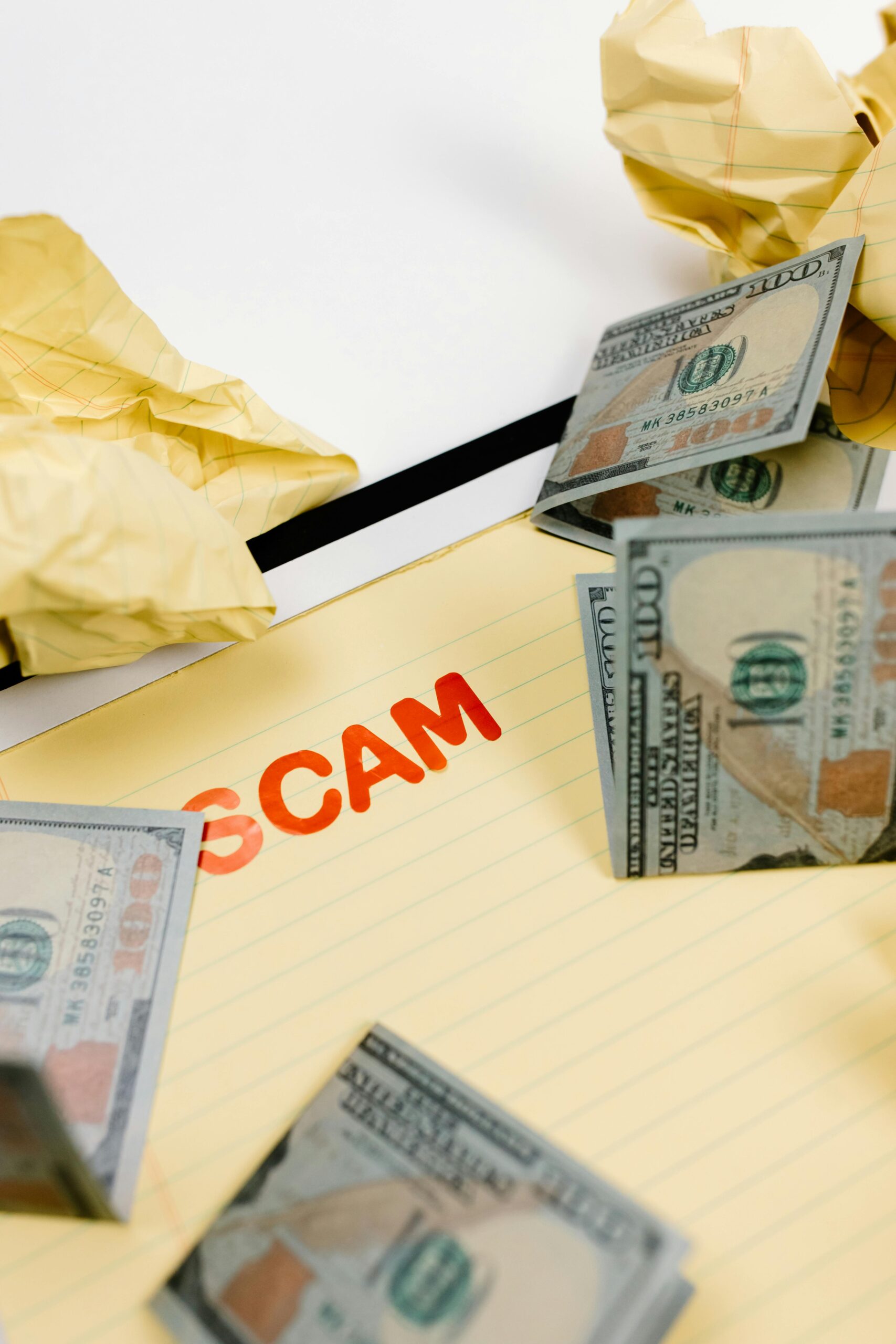 The word "scam" on a piece of paper, surrounded by money